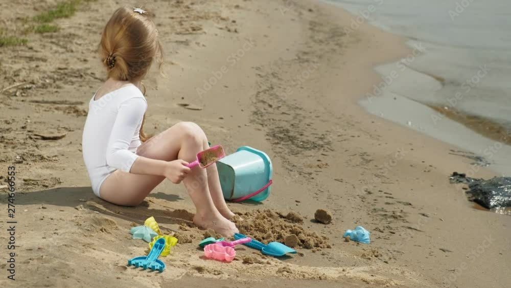 Girl child plays with sand on the beach using molds figurines. Sunny summer day. vacation Girl child plays with sand on the beach using molds figurines. Sunny summer day. vacation