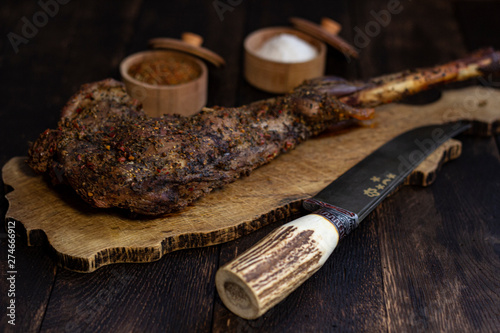 Baked goat leg on oak table with spices and knife