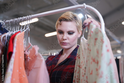 Obraz na plátně beautiful buxom girl in a fashionable dress walking in the store and chooses new clothes, looking at trendy costumes on hangers in the Mall alone