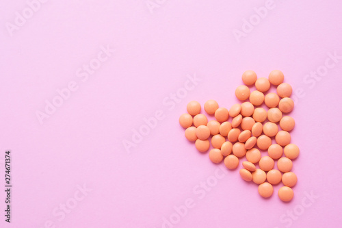 Heart made of orange tablets from glass bottle on pink background. copyspace for text. Epidemic, painkillers, healthcare, treatment pills and drug abuse concept. top view. flatlay