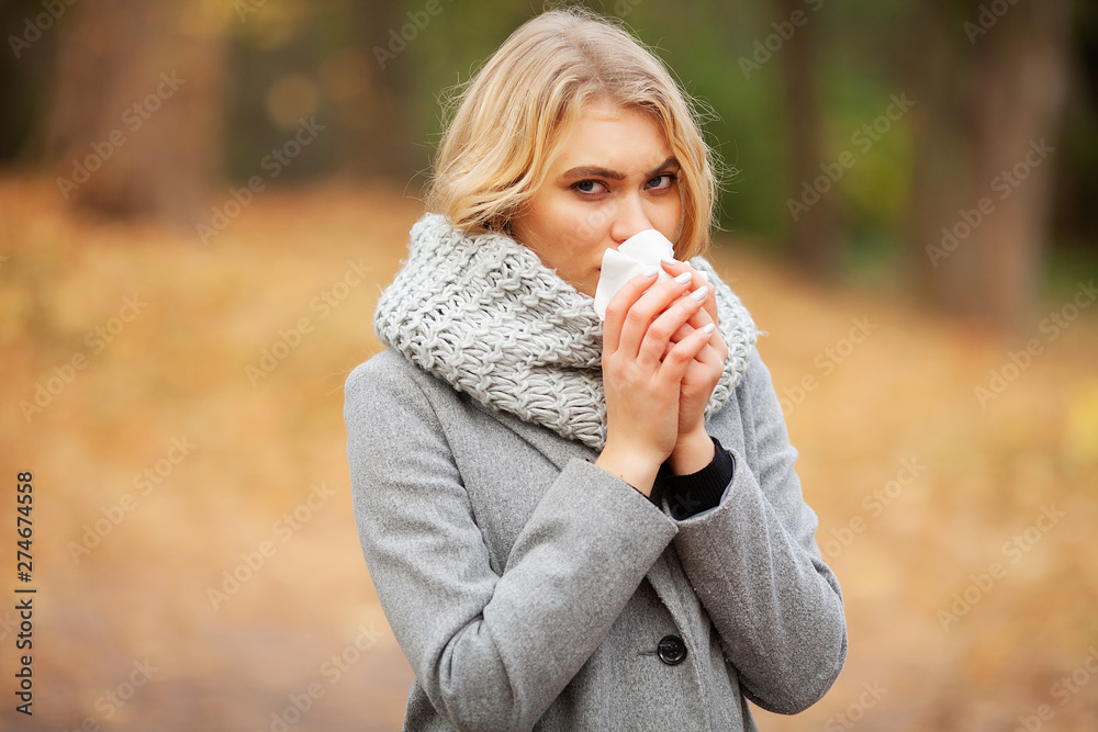 Girl sneezing in tissue. Young woman blowing her nose on the park. Woman portrait outdoor sneezing because cold and flu Girl sneezing in tissue. Young woman blowing her nose on the park. Woman portrait outdoor sneezing because cold and flu