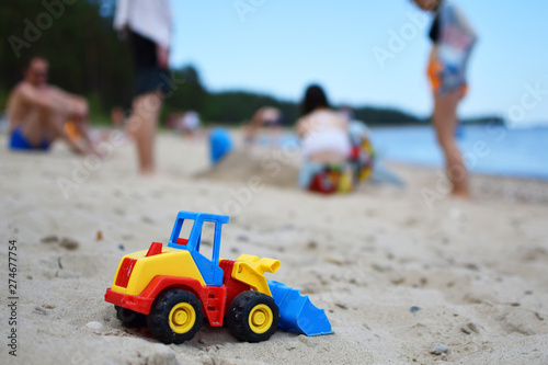 Wallpaper Mural Toy tractor bulldozer on beach sand and blurred silhouette of people and sea on background. Leisure time with friends and family and summertime vacation concept. Torontodigital.ca