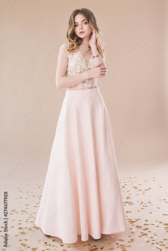 Beautiful girl in evening elegant dress posing on paper beige studio background full length portrait
