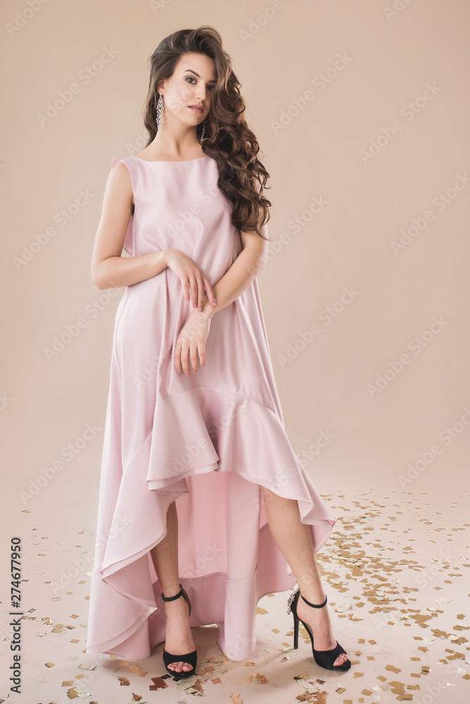 Fototapeta premium Beautiful girl in evening elegant dress posing on paper beige studio background full length portrait