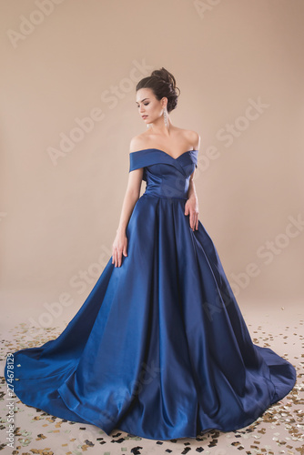 Beautiful girl in evening elegant dress posing on paper beige studio background full length portrait