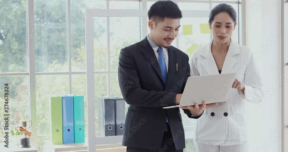 Asian business people standing, man holding notebook computer in his hand, woman checking report from screen in office. Asian business people standing, man holding notebook computer in his hand, woman checking report from screen in office.