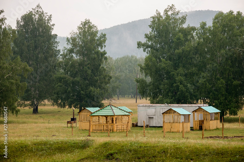 Heavy clouds in the cold autumn sky over village with small light wooden houses far away in the mountains. Wide river flows near with reflections in the water. Travelling on the suburb roads. Fog