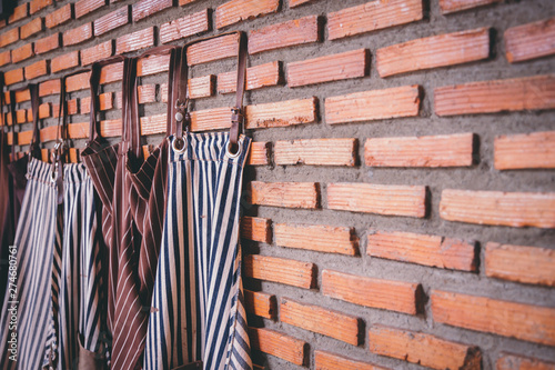 Obraz na plátně Dark-colored aprons hung together with bricks on the wall in the cafe