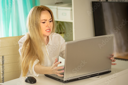 Confused young woman looking on laptop at home feeling bewildered by no connection, reading online news in internet.