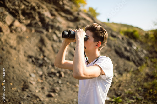 Young man holding a binoculars looking on top of mountain