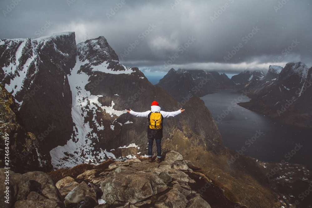 Traveler man with a yellow backpack wearing a red hat standing on the background of mountains and sea. Travel lifestyle concept. Shoot from the back