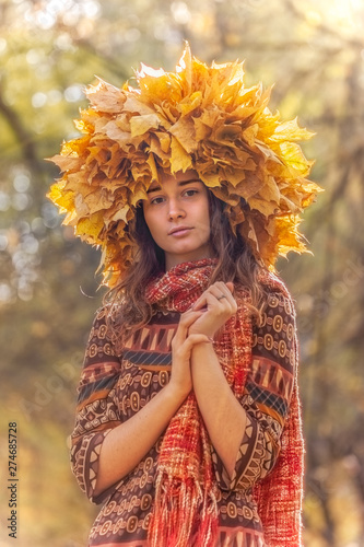 Young smiling woman with wreath of maple leaves on a head, outdoor portrait in autumn park