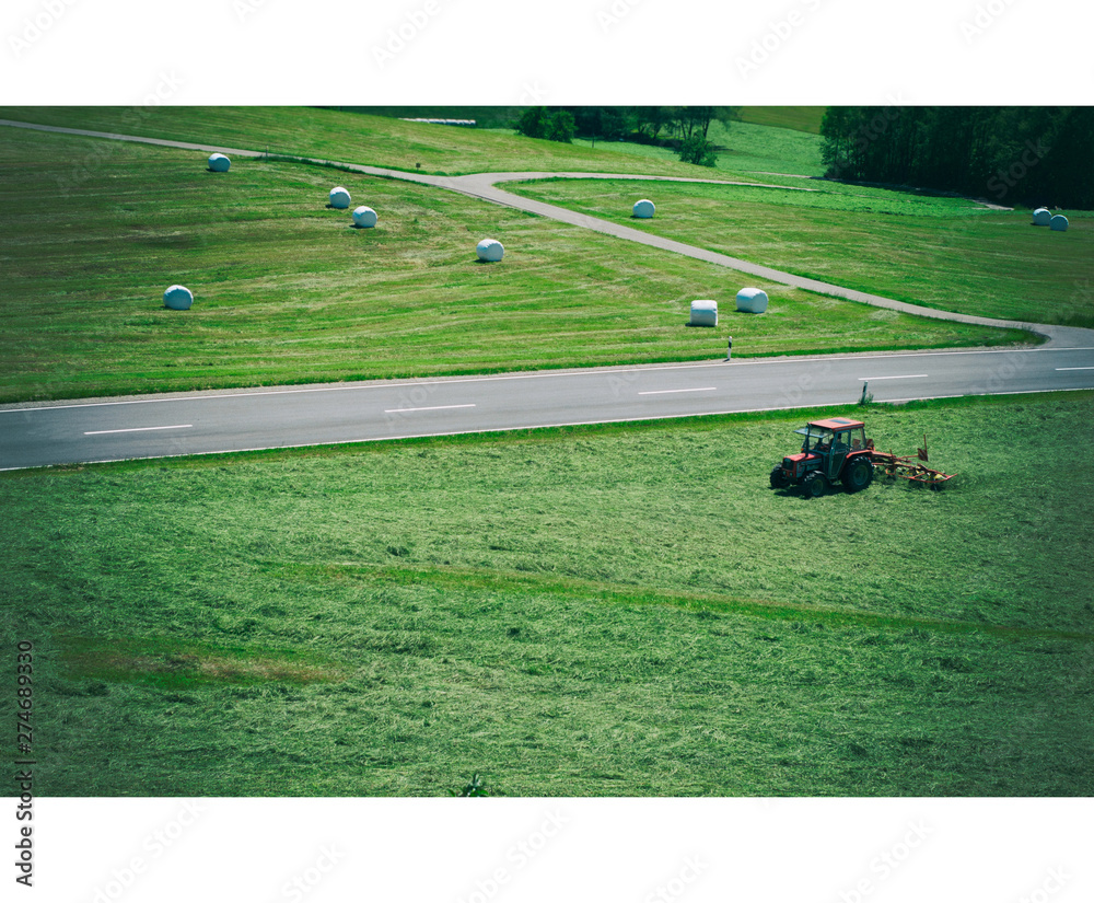 Scheidegg, Germany - June 06, 2019: The tractor turns dry grass in the field in a summer day. Rolls of packed, fresh dry hay in the fields