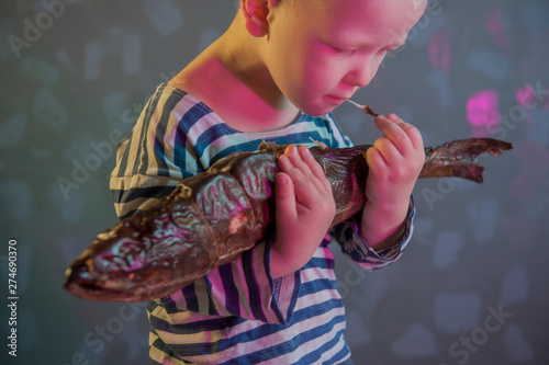 Little blond boy shows big smoked fish. Child wants to catch big fish in ariver. Concept of organic food. photo