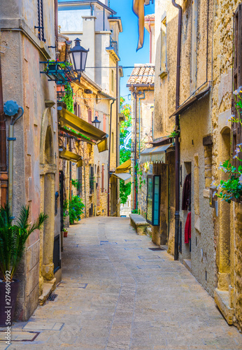Fototapeta Naklejka Na Ścianę i Meble -  Typical italian cobblestone street with traditional buildings and houses with green plants on walls in old historical city centre San Marino