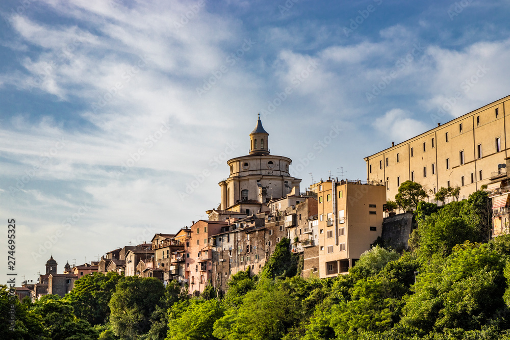 A view of the city of Zagarolo, with the houses built sheer above a tuff hill. Above the roofs the dome of the church of San Pietro appears. The valley full of trees. Province of Rome, Lazio