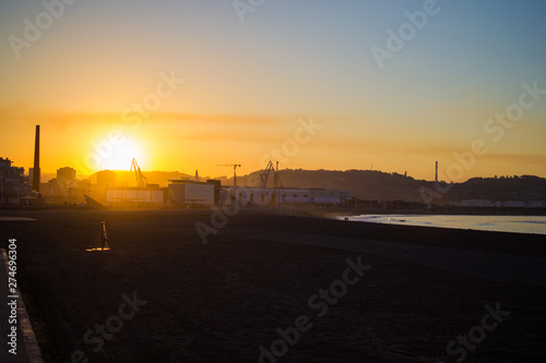Beautiful sunset in Poniente beach with the dock at the background, in Gijon, Asturias, Spain.
