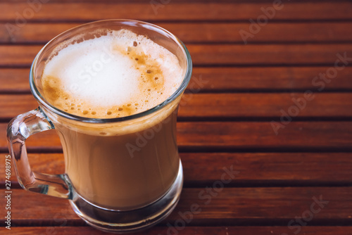 Cup or glass of coffee with white foam on wooden brown table, with copy space, top view