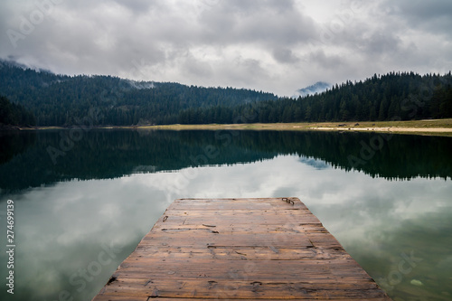 Montenegro, Wooden landing stage in calm waters of black lake surrounded by endless green forest in nature landscape of durmitor national park near zabljak