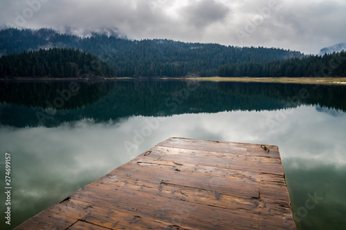 Montenegro, Wooden landing stage in perfect black lake nature landscape surrounded by green forest in misty atmosphere in durmitor national park next to zabljak