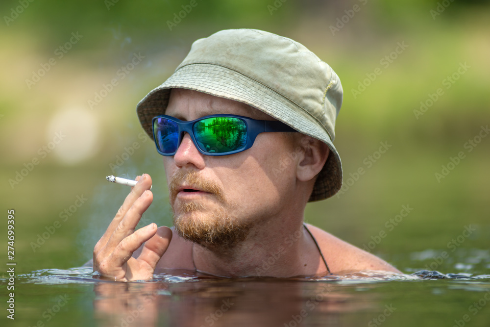 Portrait of a funny smoking a cigarette man, enjoying swimming in hat and  sunglasses. Concept vacation, active rest Stock Photo | Adobe Stock