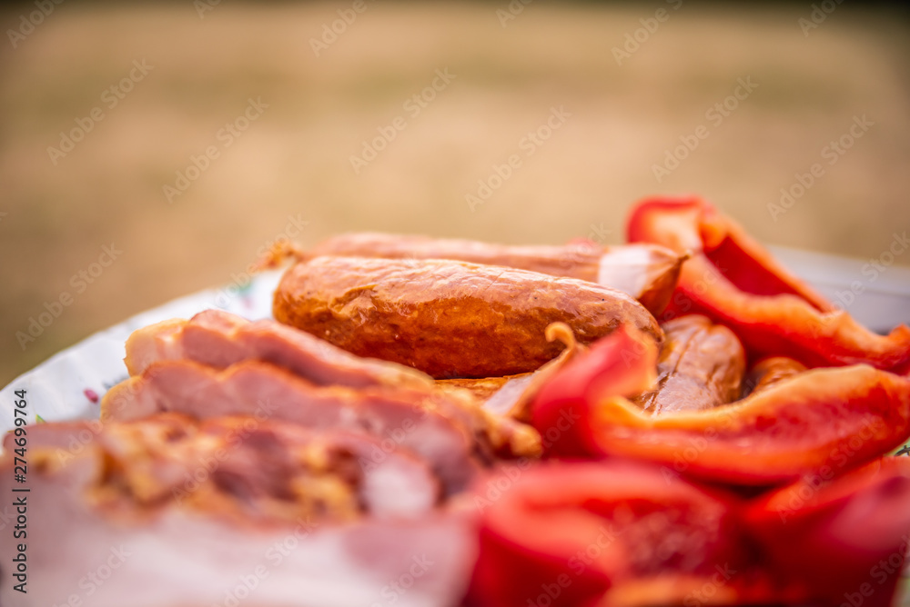 Close up of raw bacon, sausages and paprika on colorful tray, prepared for barbecue Close up of raw bacon, sausages and paprika on colorful tray, prepared for barbecue