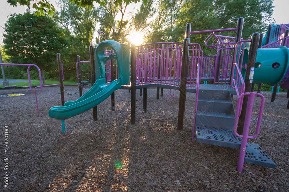 Purple and blue children's playground in the park with sun flare coming through trees Purple and blue children's playground in the park with sun flare coming through trees