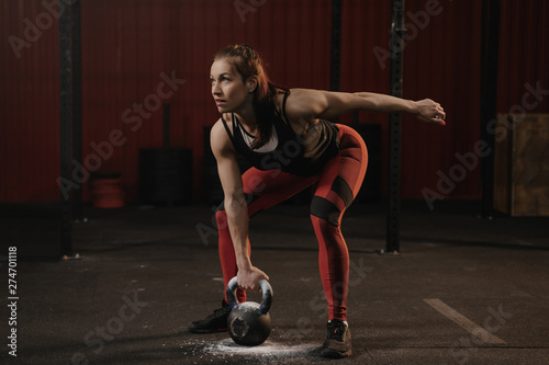 Female athlete lifting heavy weights. Sports woman holding kettlebell while crossfit training.