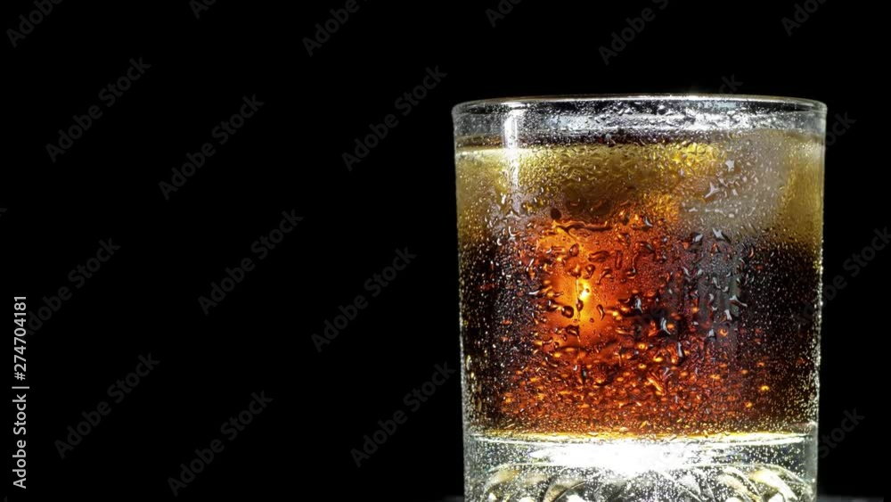 Cola with ice cubes in glass over black background. Cola with bubbles being poured in glass. Rotate glass of Cola fizzy drink isolated on black background.