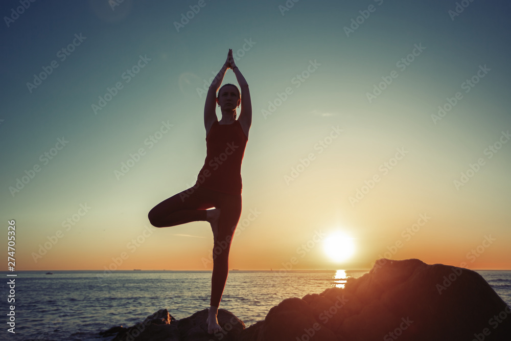 Yoga woman performs morning exercises on the seaside in the dawn.
