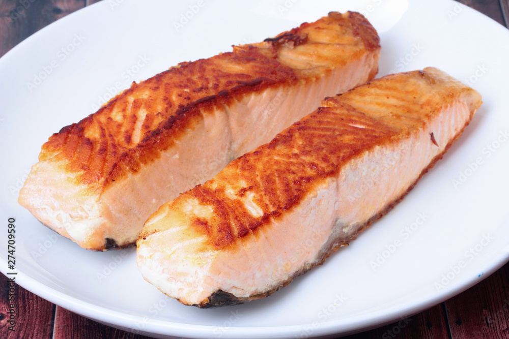 2 Grilled salmon steaks on white plate served on wood. 2 Grilled salmon steaks on white plate served on wood.
