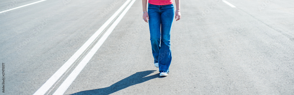 Woman legs in jeans and sneaker shoes walking on the empty road Woman legs in jeans and sneaker shoes walking on the empty road