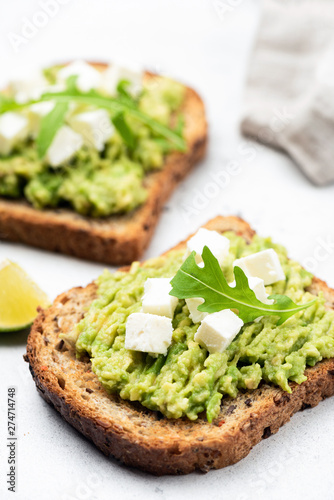 Healthy bread toast with mashed avocado and feta cheese topped with arugula leaf. Closeup view, selective focus