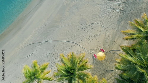Top view of the Maldives beach on a sunny evening. Green coconut palms on white sand background. Beautiful seaside postcard. Sea waves on the sand. Footprints on the sand of a deserted beach.