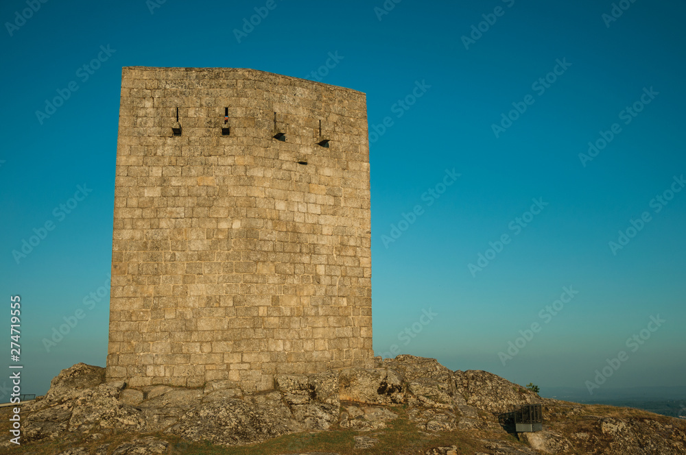 Stone square tower over rocky hill on sunset