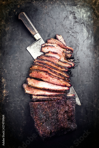 Traditional smoked barbecue wagyu beef brisket offered as top view with a knife on an old rustic board with copy space