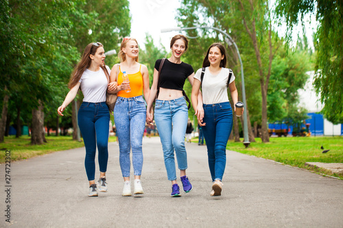 Happy women in blue jeans walking in summer park