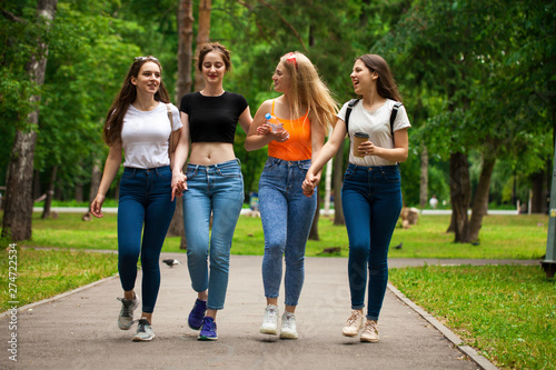Happy women in blue jeans walking in summer park