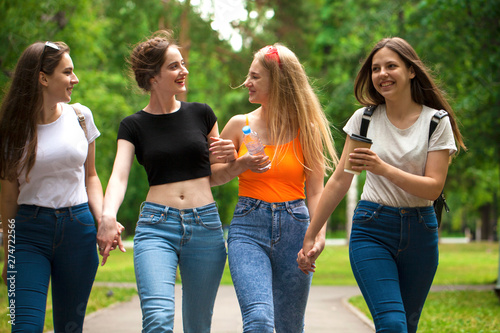 Four happy schoolgirls walking in summer park