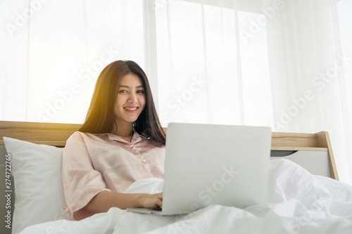 Portait of smiling lady in pink pajama wake up searching information in notebook on the bed
