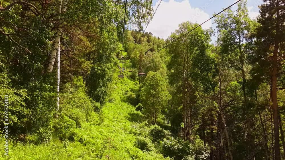 Panorama aerial view on ropeway. Chairlift in forest. Movement on Cableway in summer through the forest. Moving the funicular to the mountain