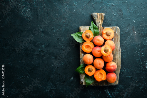 Fresh apricots with green leaves on a black background. Rustic style. Top view. Free space for your text.