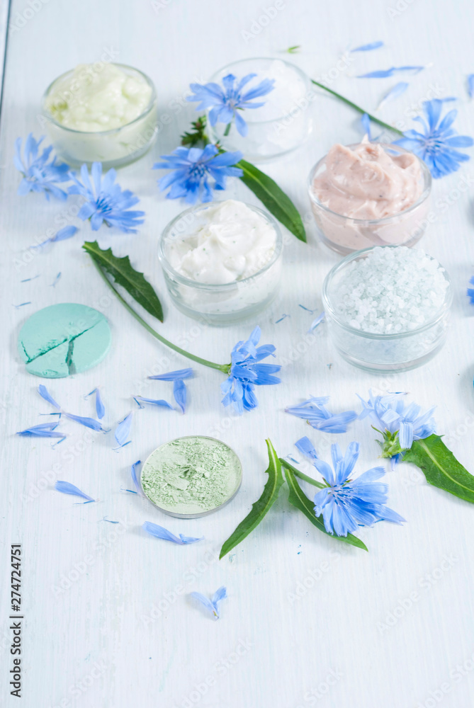 moisturizers, bath salts and powder compacts with blue chicory flowers on white wood table