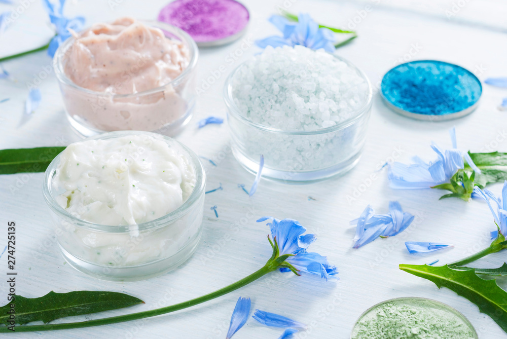 moisturizers, bath salts and powder compacts with blue chicory flowers on white wood table moisturizers, bath salts and powder compacts with blue chicory flowers on white wood table