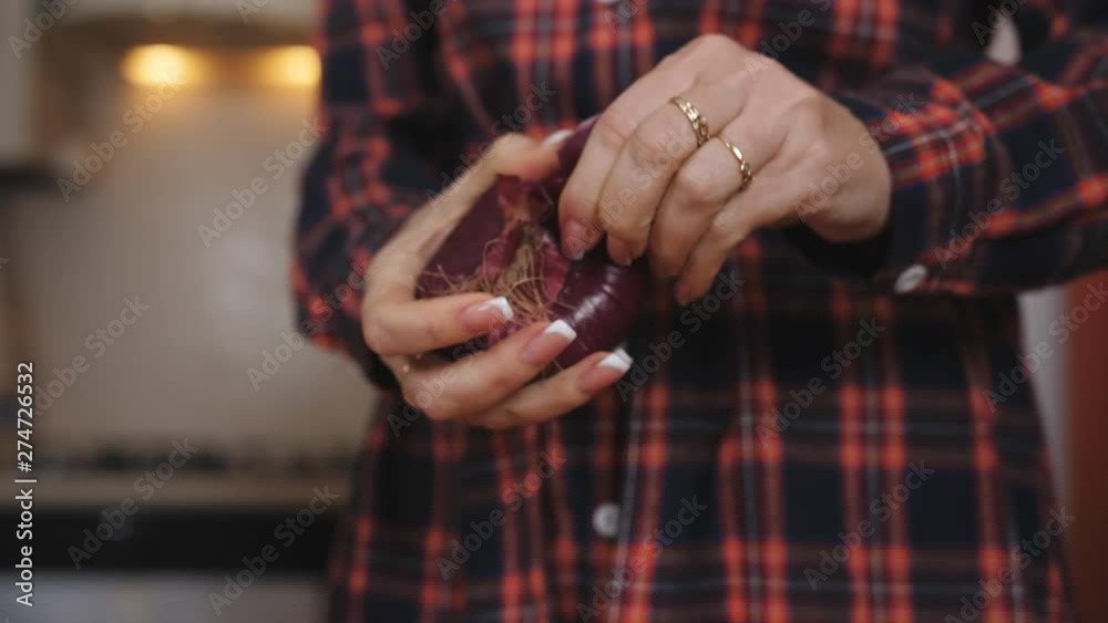 Woman peels a red onion by hands and knife.