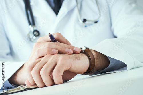 Man doctor with stethoscope looking at wrist watch. Doctor in white uniform at office background waiting for patients. Time to visit therapist.