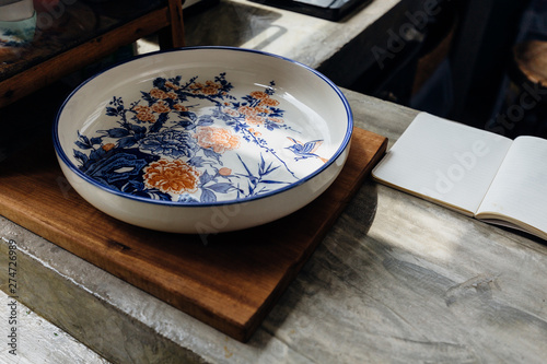 Chinese traditional decorative ceramic plate on wooden block with open notebook on kitchen counter. photo