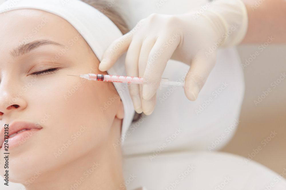 Female cosmetologist makes beauty shots to her client woman sitting on a couch. Concept of rejuvenating aesthetic salon procedures Female cosmetologist makes beauty shots to her client woman sitting on a couch. Concept of rejuvenating aesthetic salon procedures