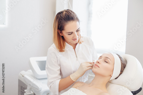 Female cosmetologist makes beauty shots to her client woman sitting on a couch. Concept of rejuvenating aesthetic salon procedures