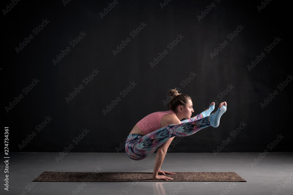Young european woman practices yoga hand balance asana titibhasana or firefly pose on dark background Young european woman practices yoga hand balance asana titibhasana or firefly pose on dark background